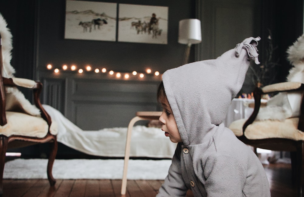 toddler wearing gray hoodie sitting in the floor