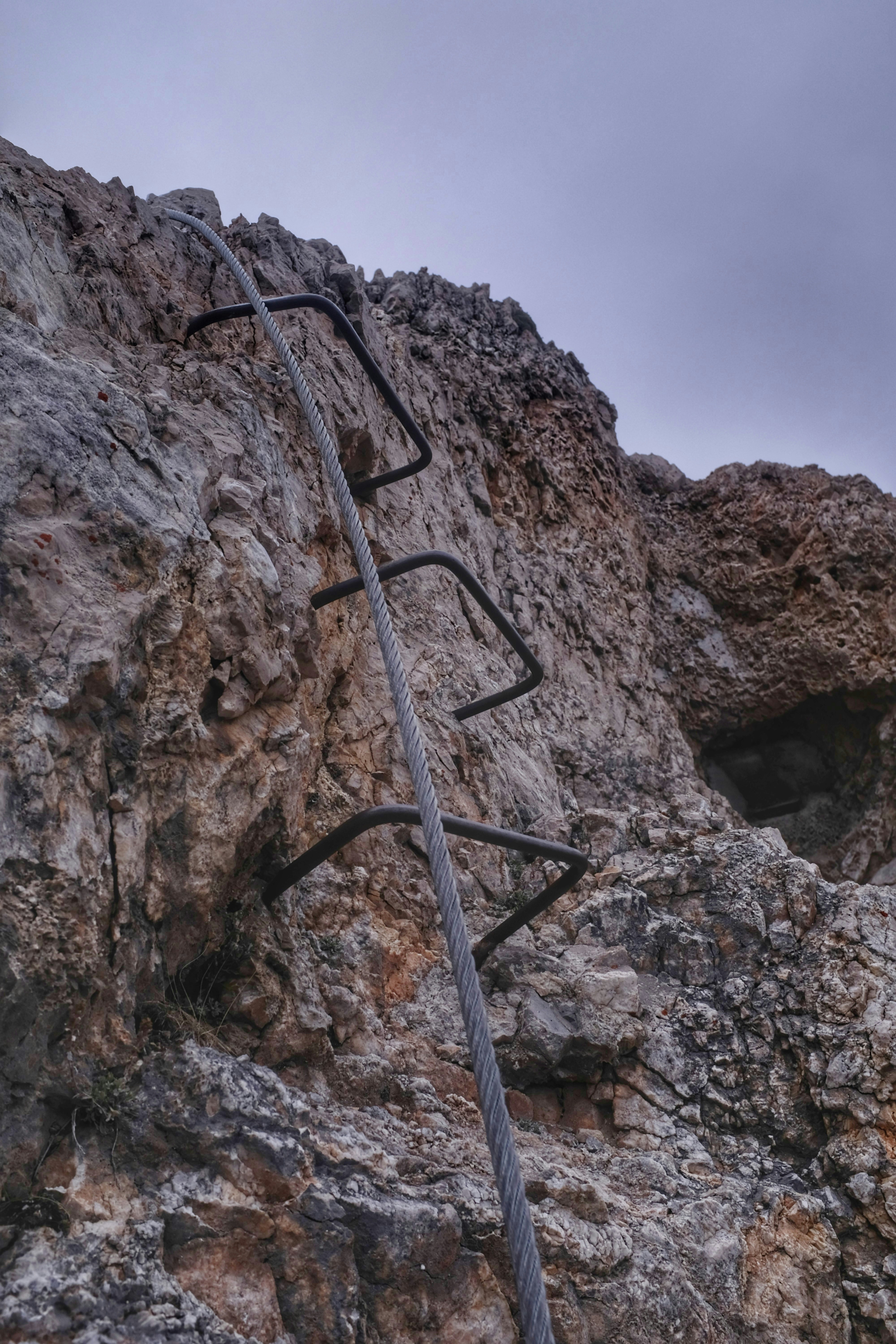 Climber ascending iron rungs on vertical Dolomite rock face with valley far below