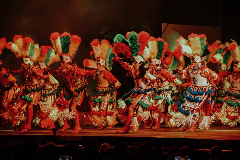 Performers from Grupo Estirpe dancing energetically on stage with colorful traditional costumes and dynamic lighting.