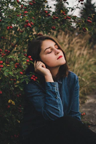 A woman sitting peacefully in nature, reflecting with a gentle smile.