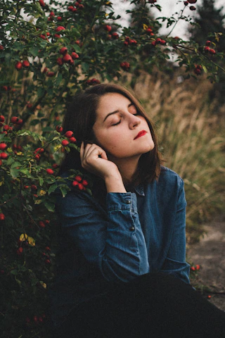 A serene woman smiling softly while sitting outdoors, embodying peace and healing.