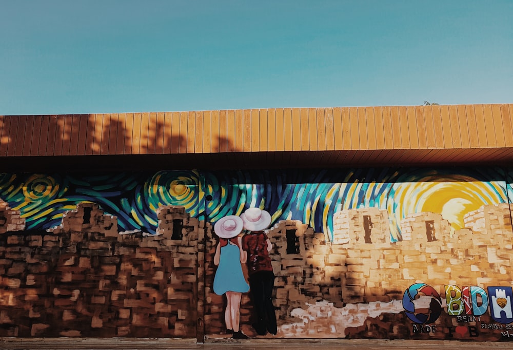 two women looking from a stonewall mural painting