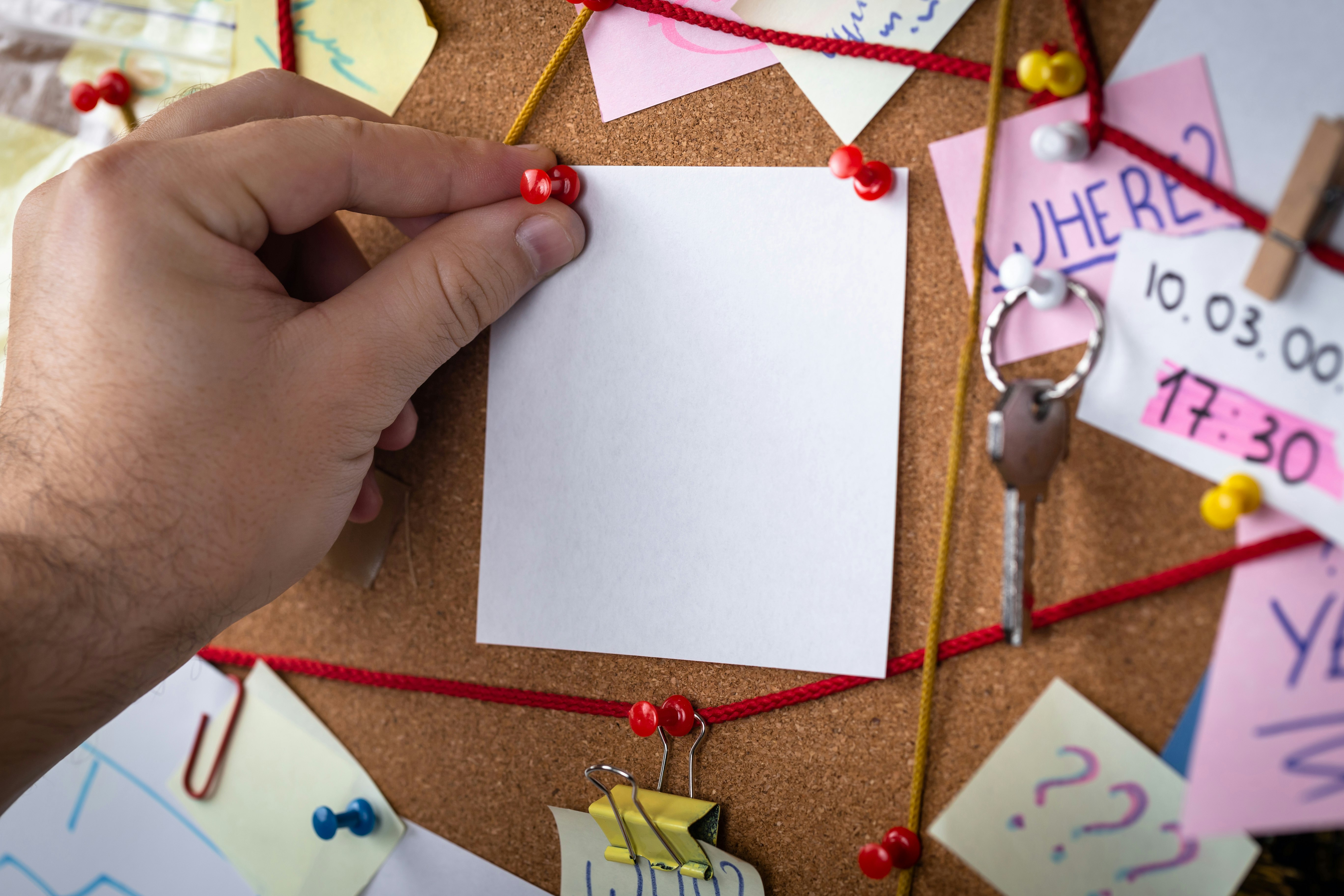 search concept. Close-up view of a detective board with evidence. In the center is a empty mock up white sheet attached with a red pin