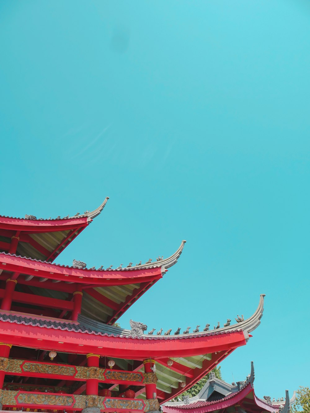 low-angle photography of red and green pagoda building under a calm blue sky