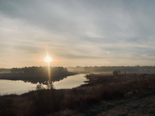 A serene landscape at dawn where a reporter takes notes beside a quiet river.