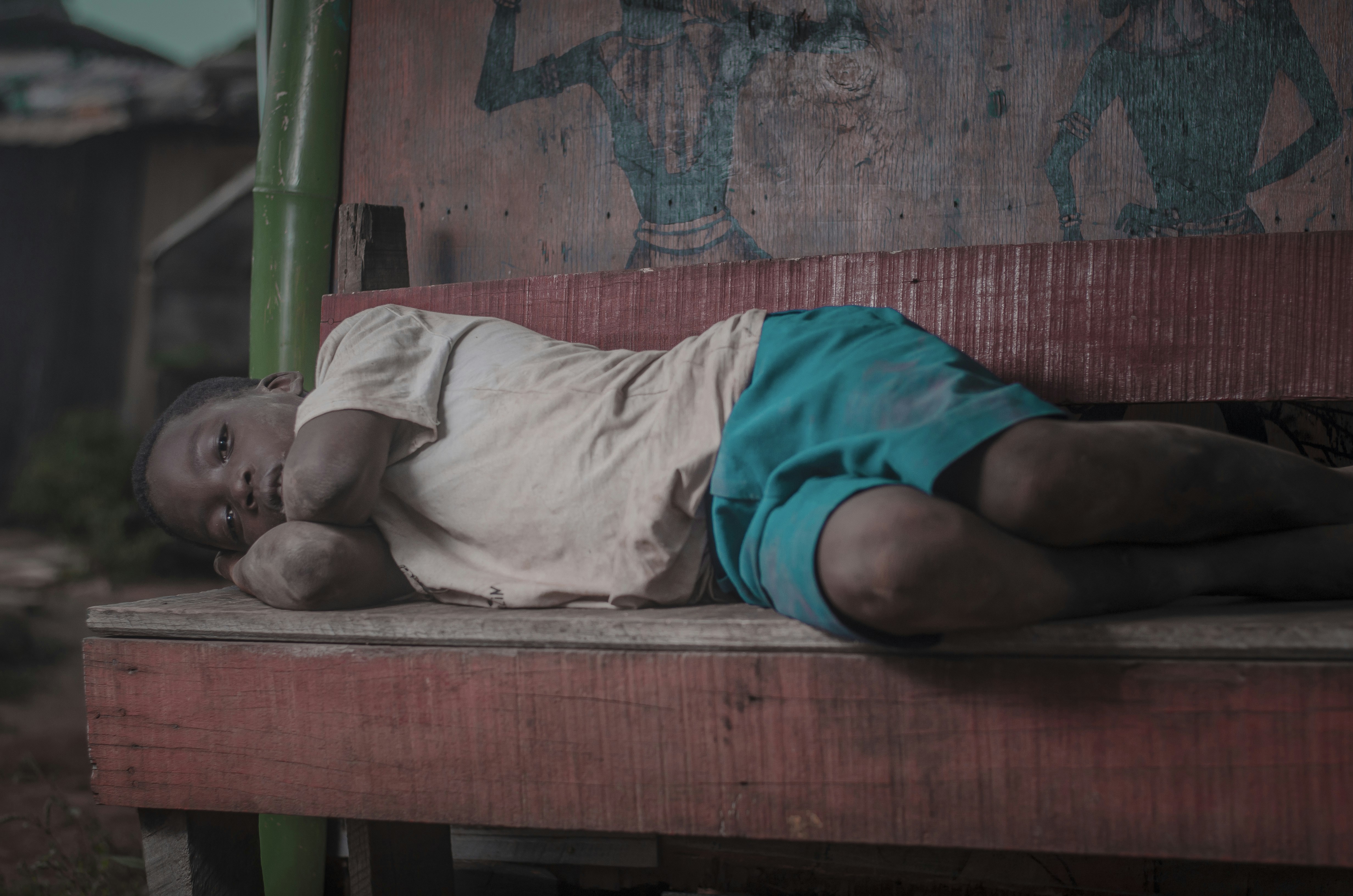 boy lying on brown wooden bench outdoors