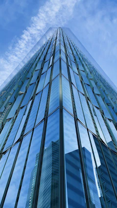 low-angle photography of blue glass walled high-rise building under blue and white sky