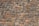 A neatly arranged stone wall with variously sized and colored rectangular stones. The stones have an uneven surface, and their colors range from shades of gray to hints of orange and brown. The mortar between the stones is visible and evenly applied.