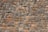 A neatly arranged stone wall with variously sized and colored rectangular stones. The stones have an uneven surface, and their colors range from shades of gray to hints of orange and brown. The mortar between the stones is visible and evenly applied.