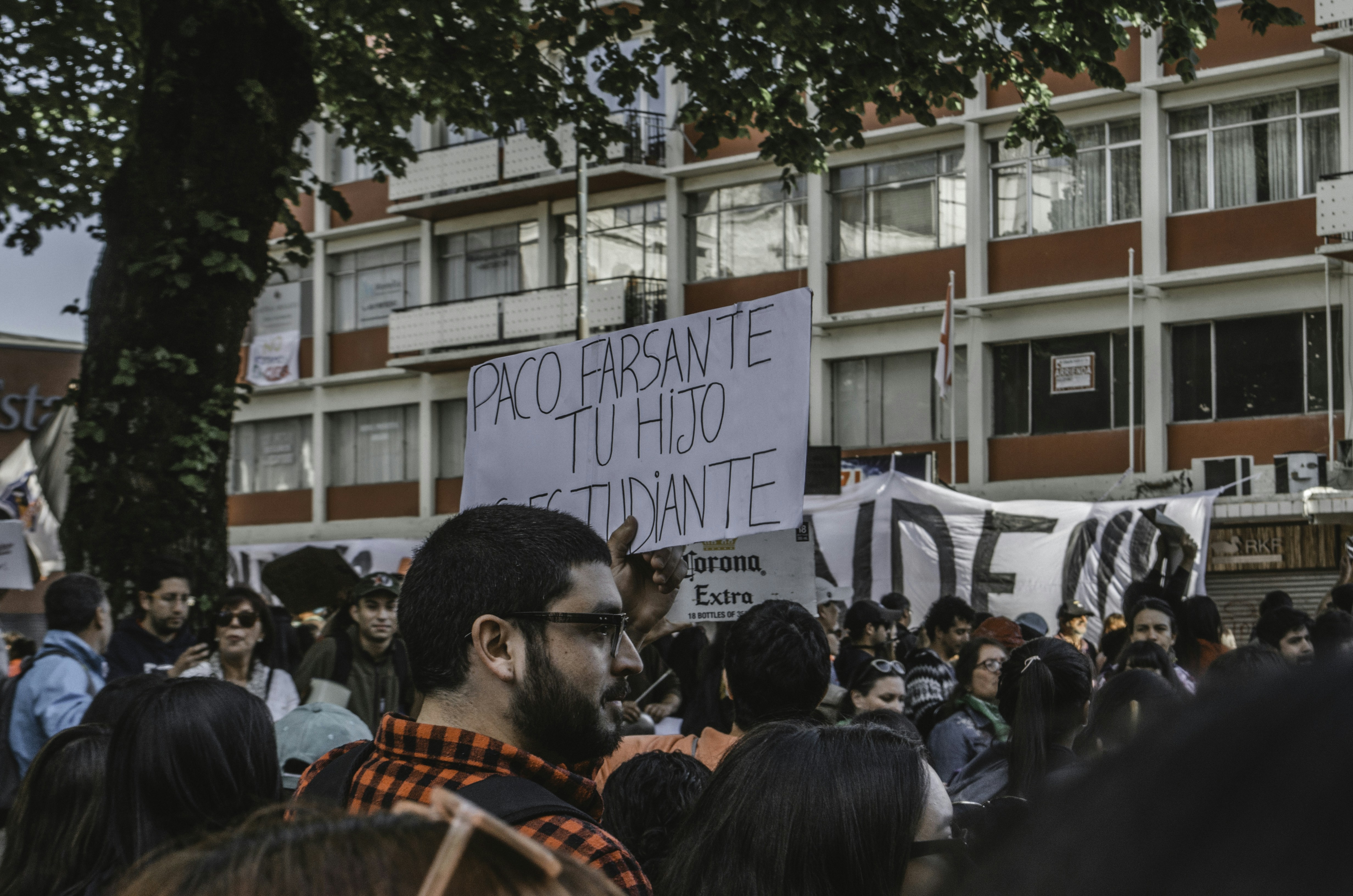 A dynamic shot of a group of university students protesting peacefully, holding banners with Hindi slogans related to jobs and education, with police personnel in the background.