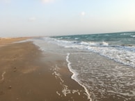 A serene beach at sunrise, waves gently lapping the shore with footprints in the sand.