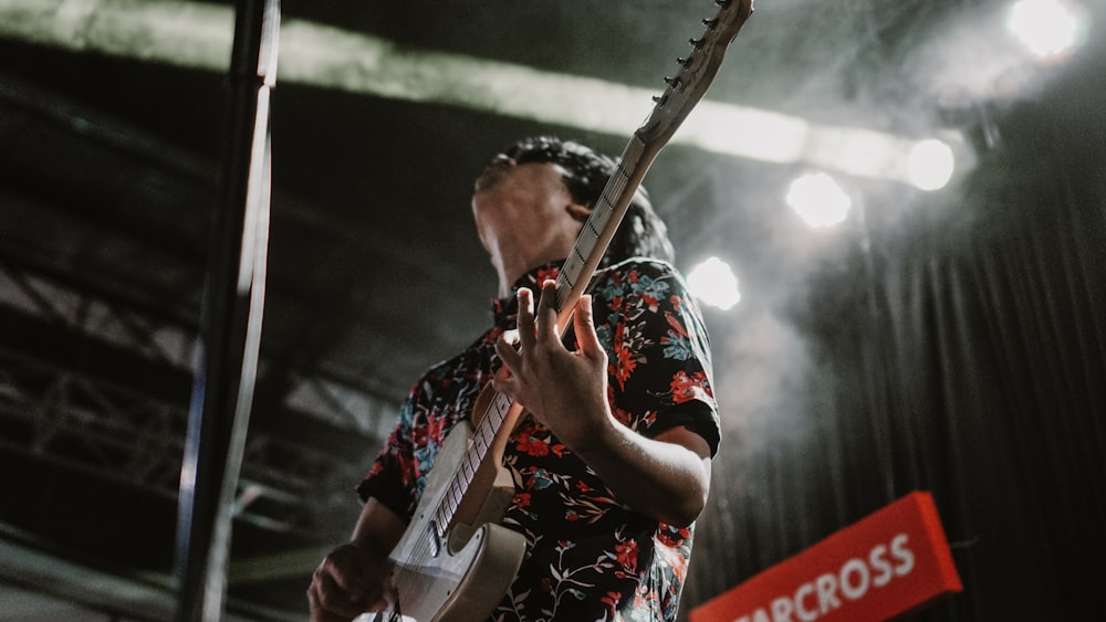 hombre vestido con camisa abotonada con cuello floral negro y rojo de pie mientras toca la guitarra eléctrica