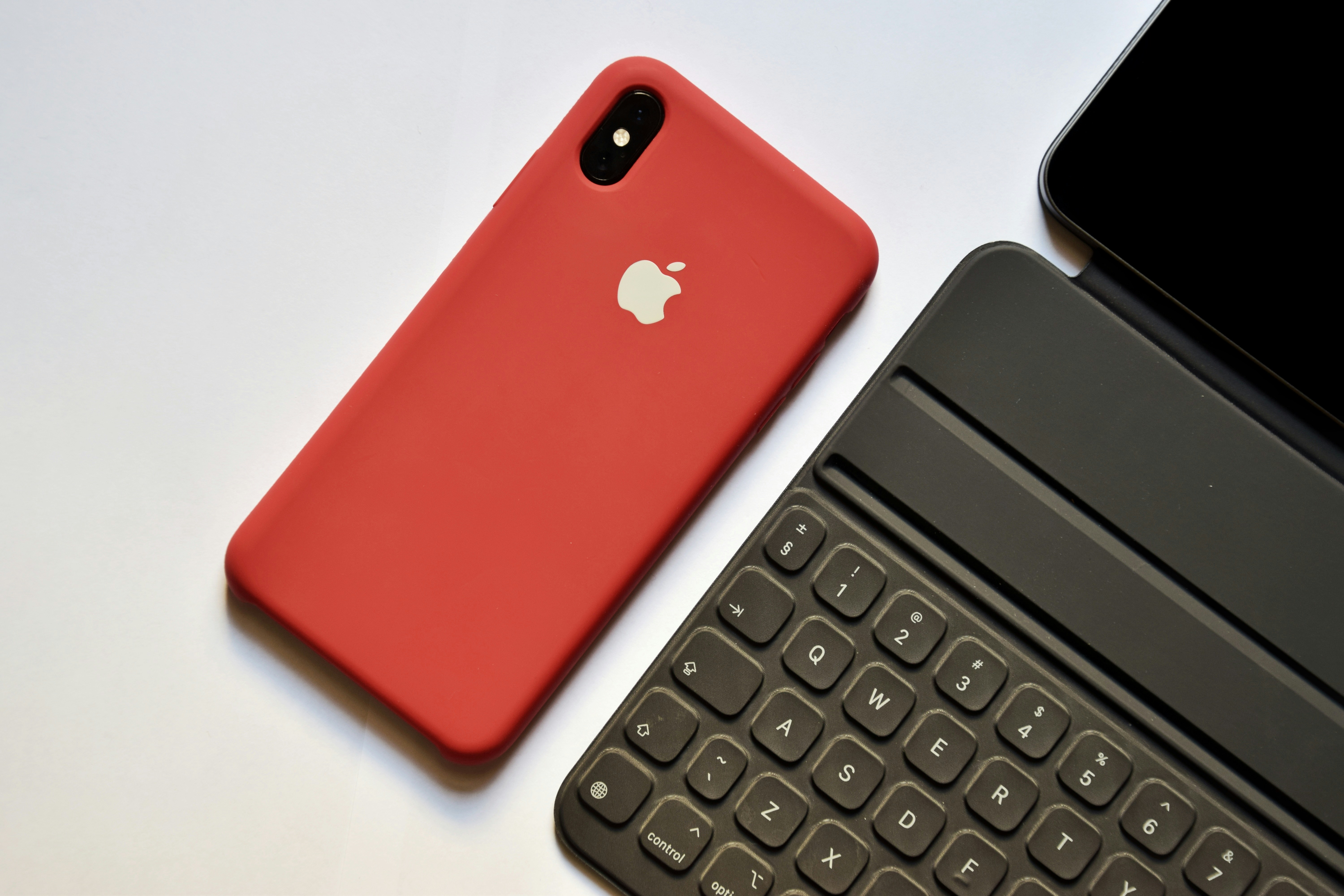 space gray iPhone with red case beside tablet keyboard
