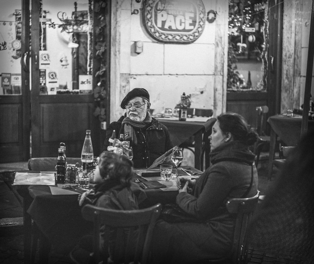 grayscale photography of three people sitting beside table