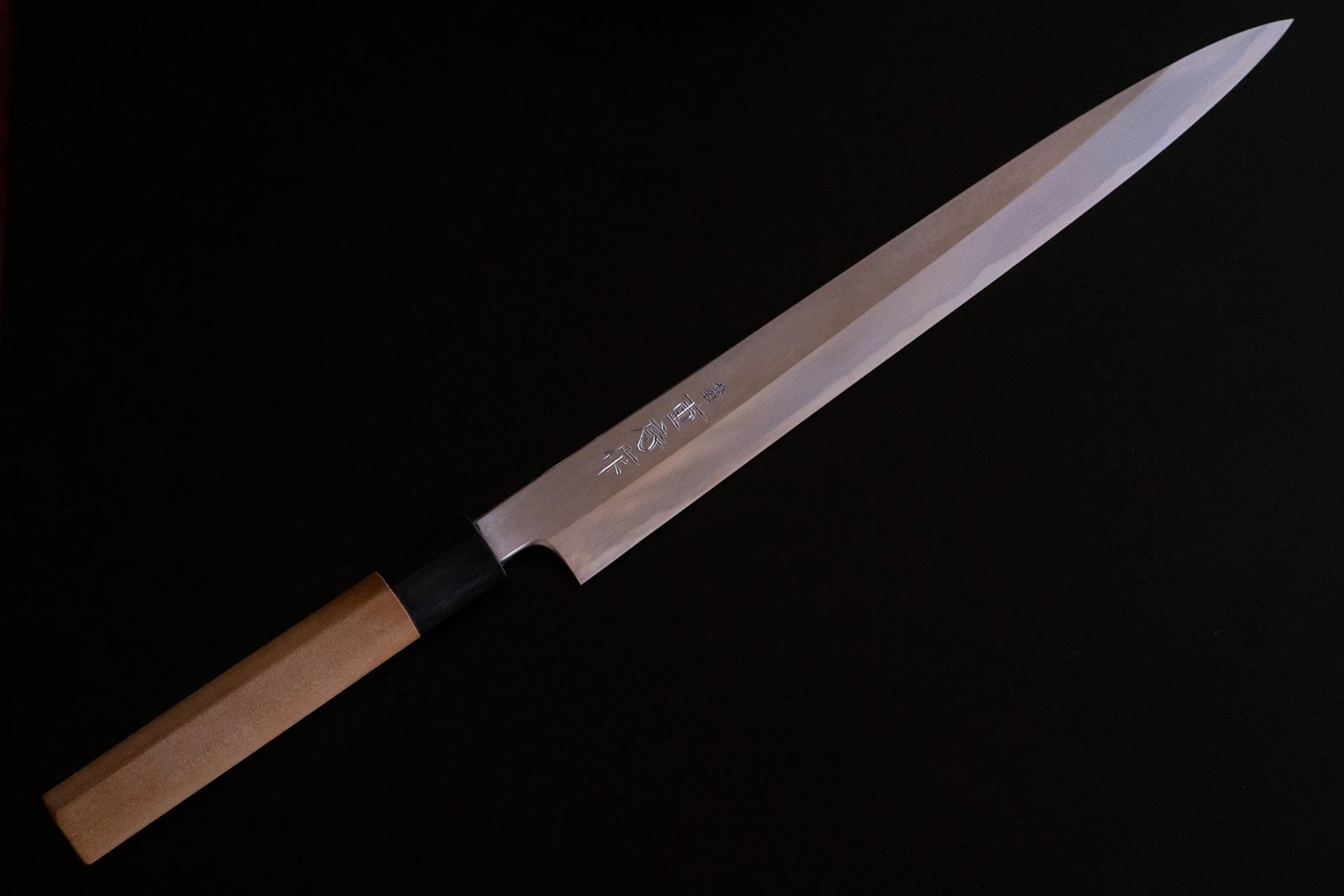 Japanese yanagiba slicing knife with a wooden handle on a black ground