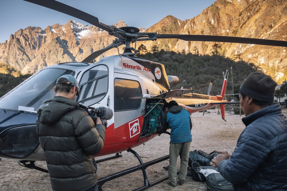 man standing beside gray and red helicopter during daytime