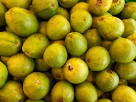 A collection of ripe, green guavas piled together, showing slight variations in texture and some surface blemishes.