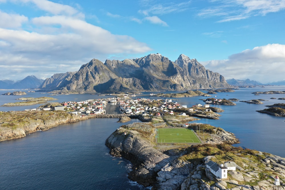 aerial photography of houses on field near body of water viewing mountain under white and blue sky