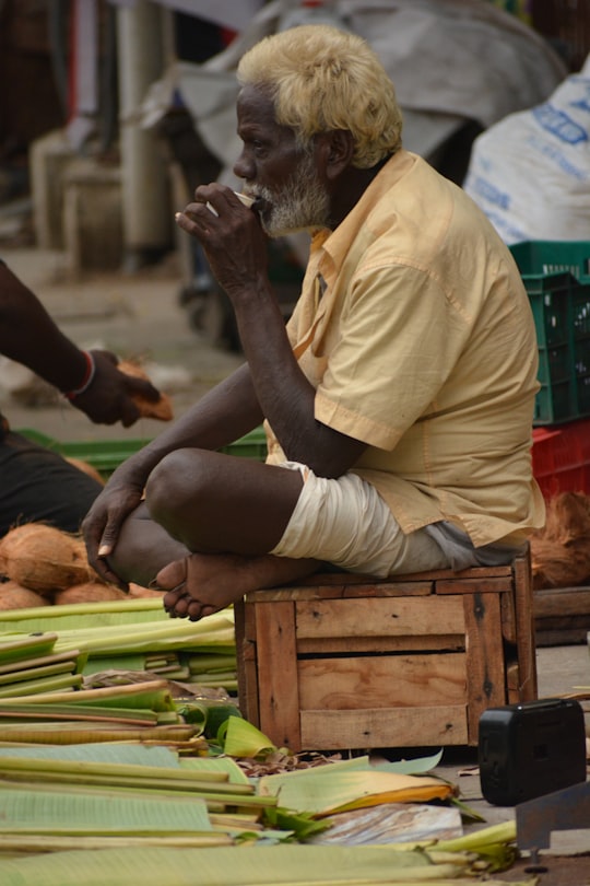 man wearing yellow shirt sitting on wooden crate in Mylapore India