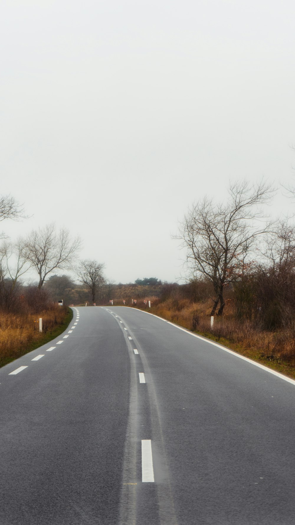 gray concrete road between brown grass field during daytime