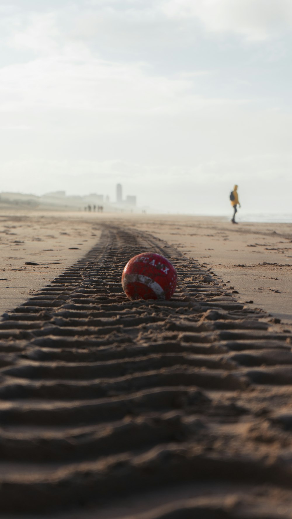 昼間の茶色の砂浜に赤と白のサッカーボール