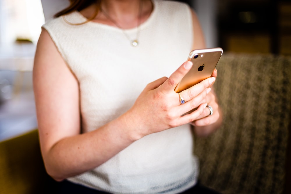 shallow focus photo of person in white sleeveless shirt holding gold iPhone 7