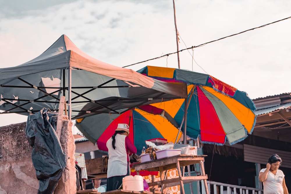 woman beside table with foods under parasol near walking woman and building during day