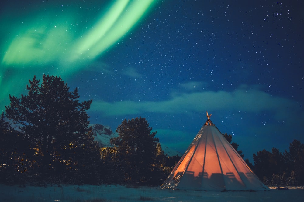 tipi tent on snowfield near trees during night