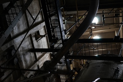 An industrial setting with metal grates, a large pipe, and various structural components. The scene is dimly lit, casting shadows and creating a moody, mechanical atmosphere.