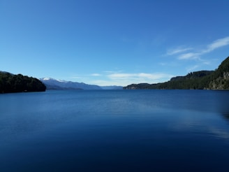 A peaceful mountain lake reflecting the clear blue sky surrounded by lush greenery.