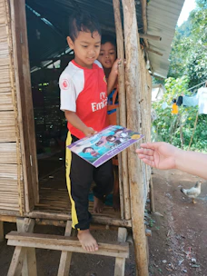 Volunteers distributing educational books to smiling children in a rural village.