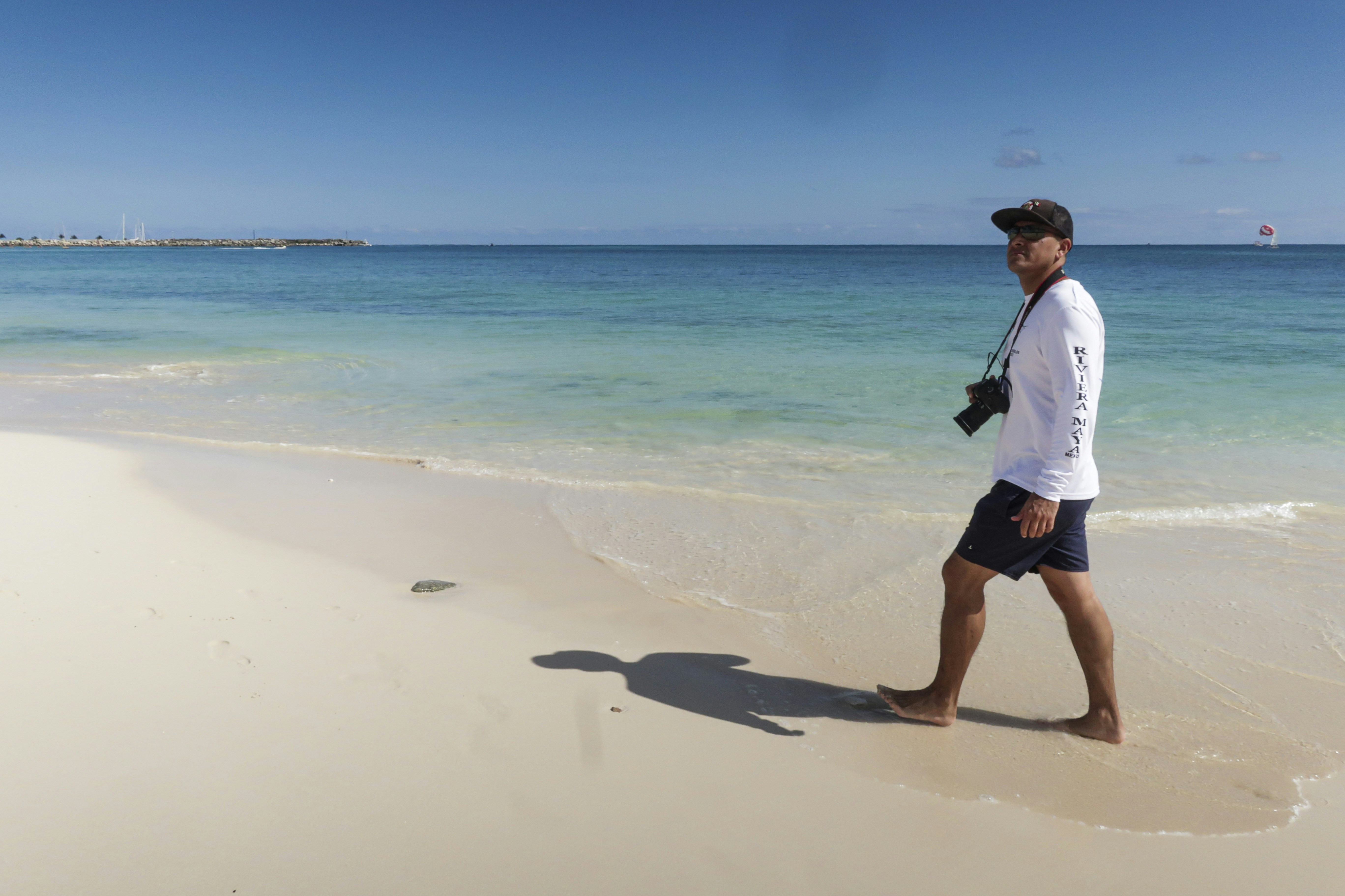 man walking at the beach with camera strap to his neck during day, 