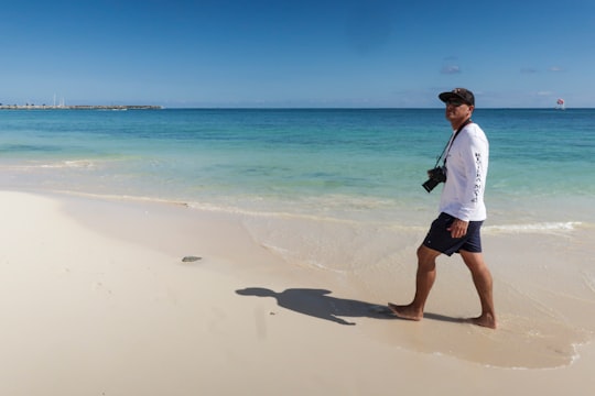 man walking at the beach with camera strap to his neck during day in Puerto Morelos Mexico