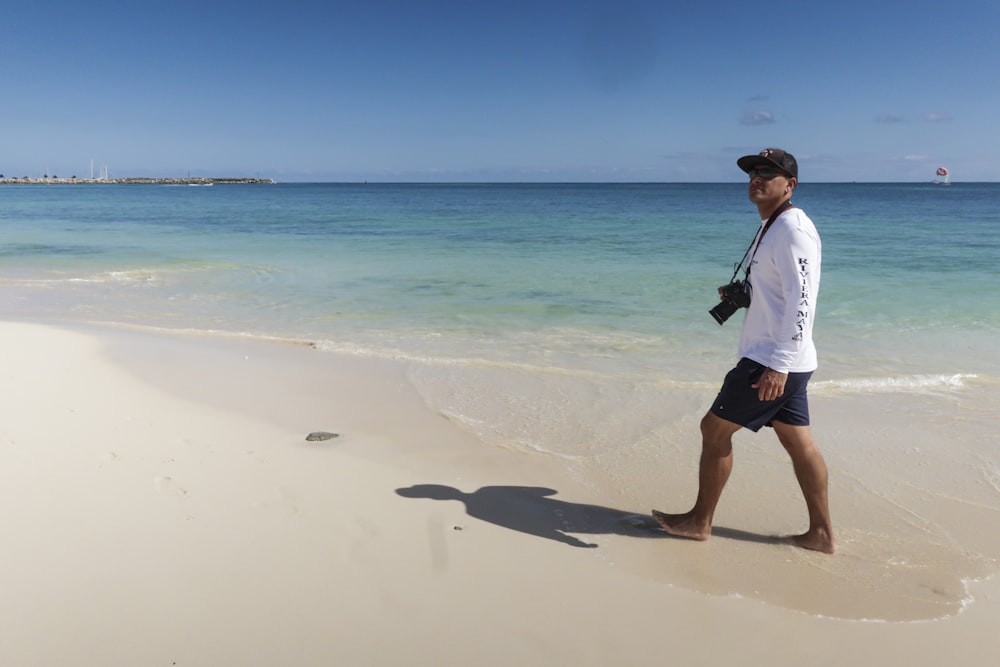 man walking at the beach with camera strap to his neck during day