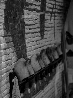 An arrangement of wooden shoe molds is mounted on a brick wall. The molds are aged and have a rustic appearance, creating a pattern of shadows on the textured wall. A cloth is hanging at the end of the rack.