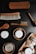 A collection of grooming products is displayed, including various brushes with wooden handles and soft bristles. There are also containers labeled as 'CLEAN + HYDRATE,' 'POLISH,' and 'WAX,' along with wooden bowls holding these products. Natural elements such as nuts or seeds are arranged on a wooden tray.