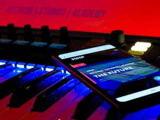 A smartphone displays a web page with the text 'THE FUTURE' and 'RECORDS / STUDIOS / ACADEMY' while placed on an illuminated music keyboard. The background features a bright red sign that also reads 'RECORDS / STUDIOS / ACADEMY'. The environment has a futuristic and technologically advanced feel.