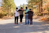 four people with hands on shoulders standing on road during daytime