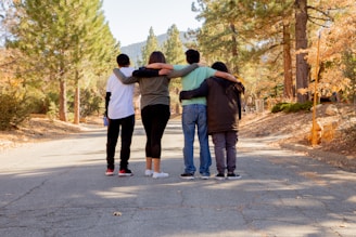 four people with hands on shoulders standing on road during daytime