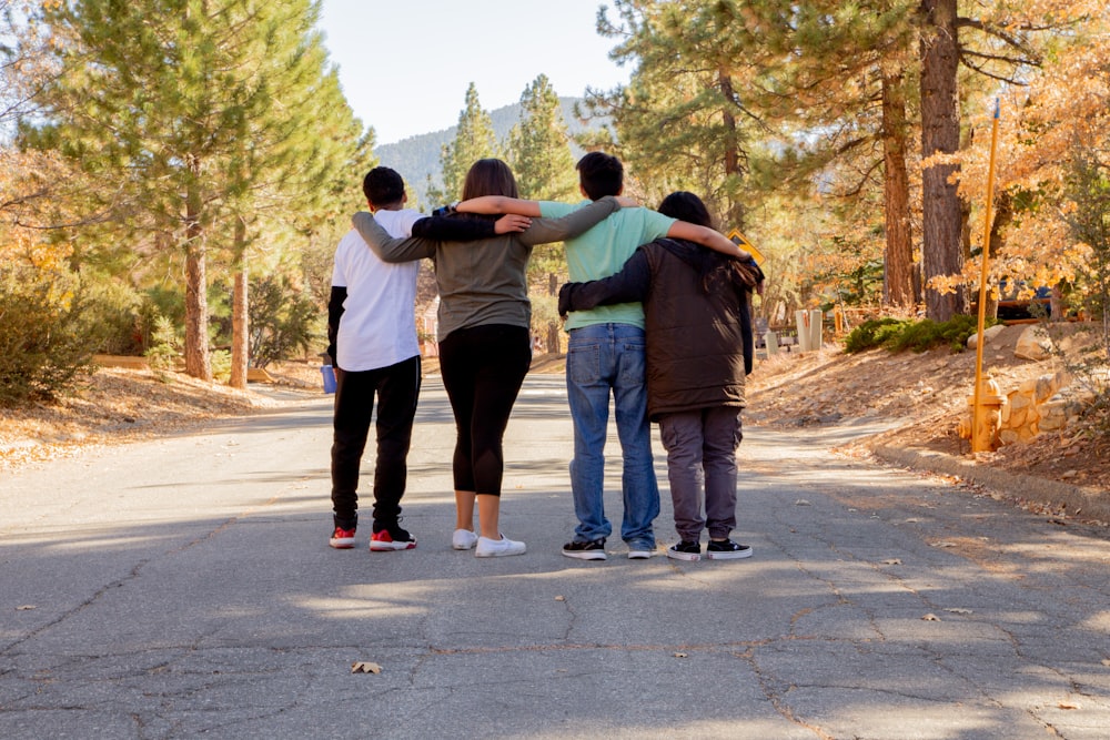 four people with hands on shoulders standing on road during daytime