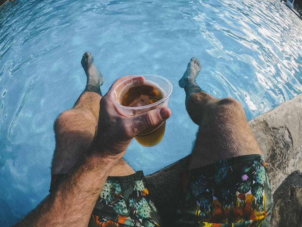 man holding a cup of drink while dipped in the swimming pool