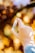 A hand holding a small tube of hemp oil balm with a blurred background of autumn leaves in shades of orange and yellow.