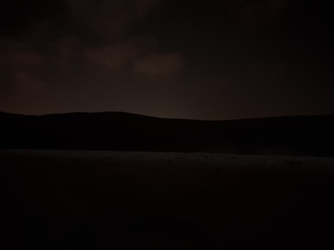 A cinematic landscape with a black sky and faint gold horizon glow.