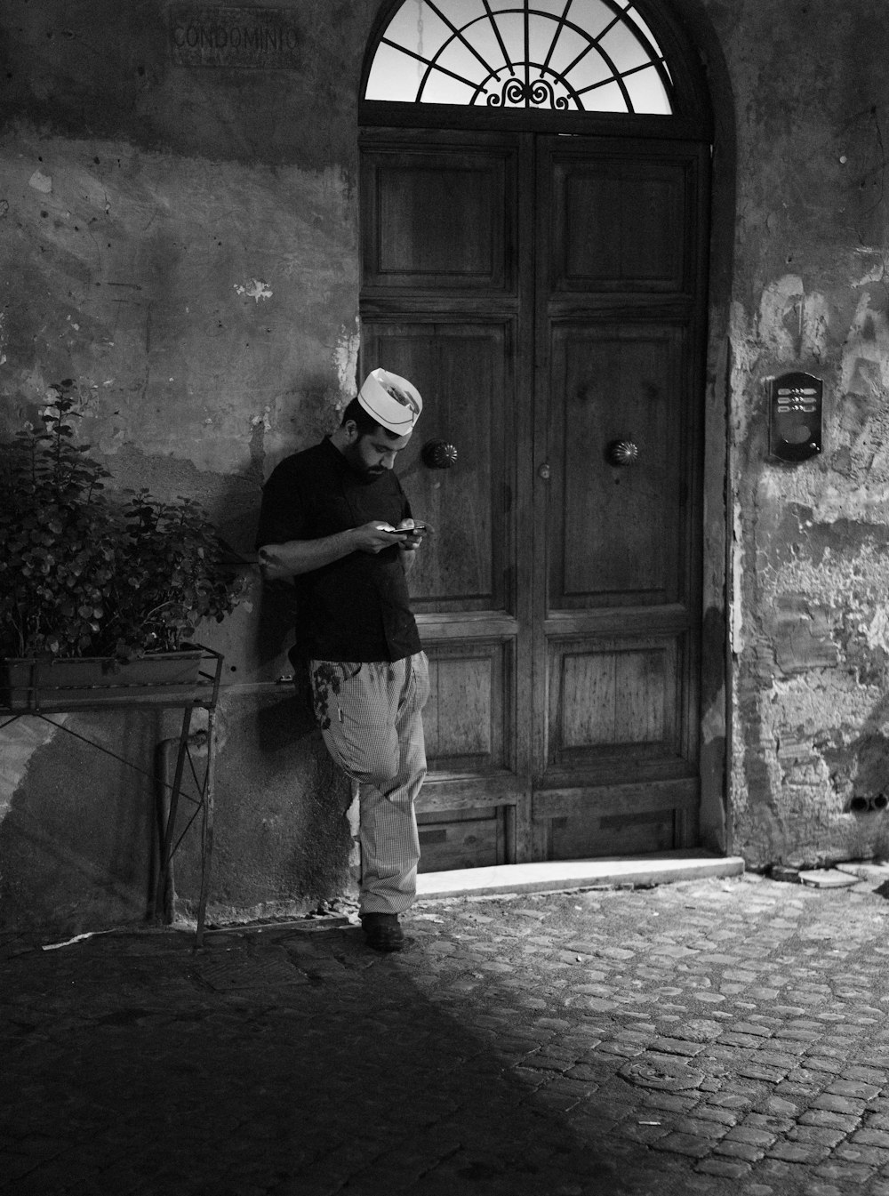 grayscale photo of man standing beside wooden door