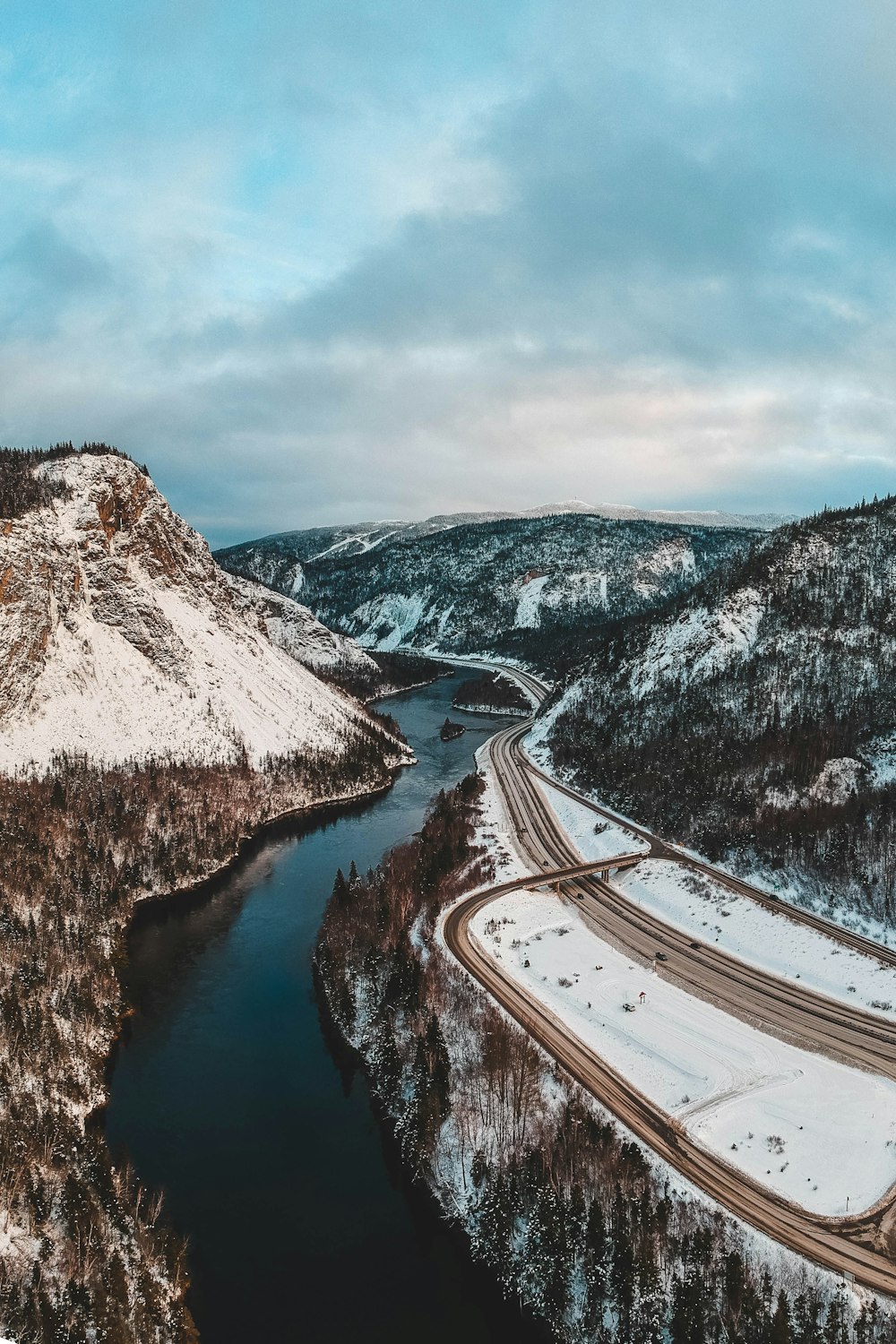 road near river and mountain covered with snow during daytime