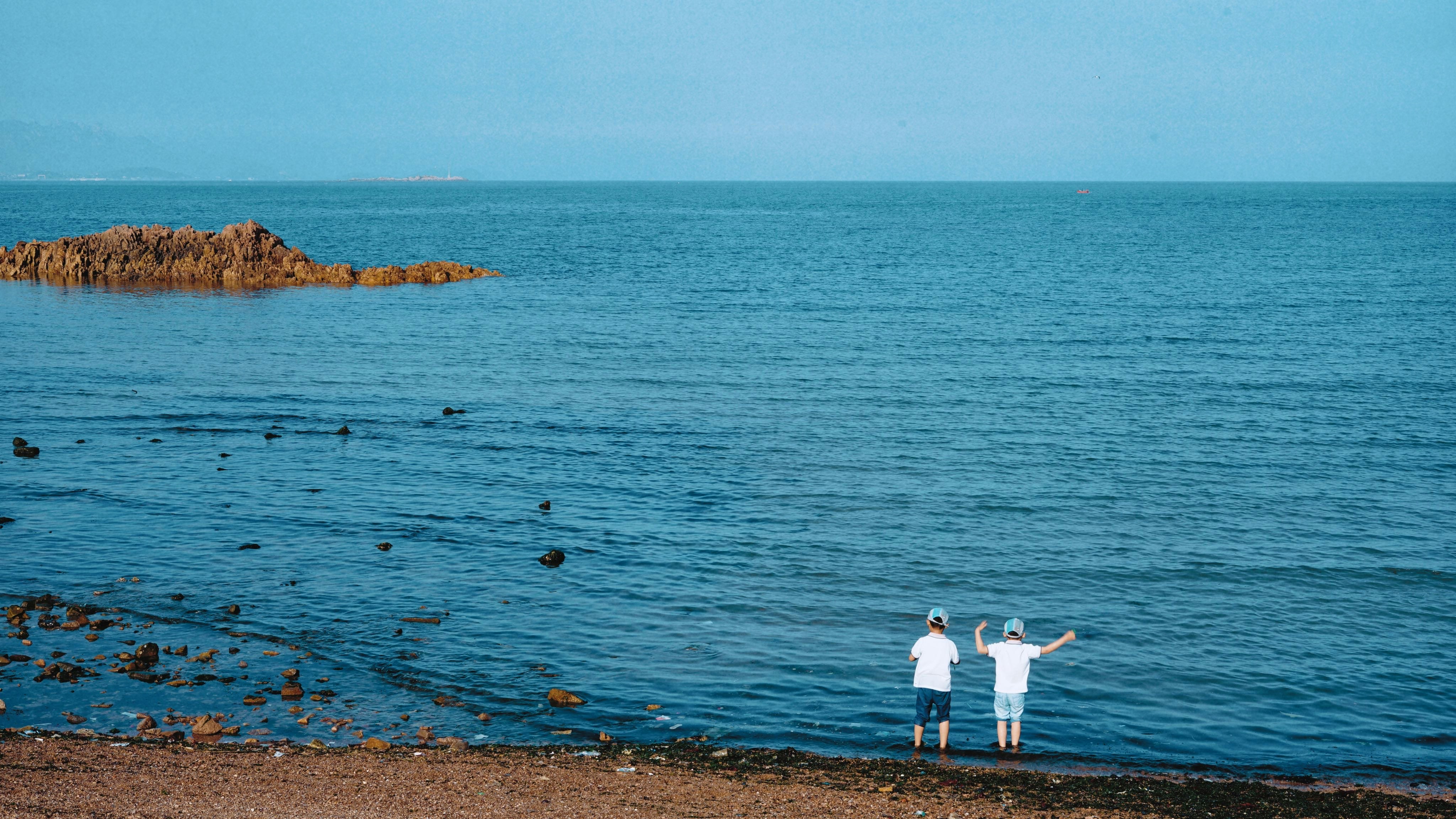two children standing in front of body of water