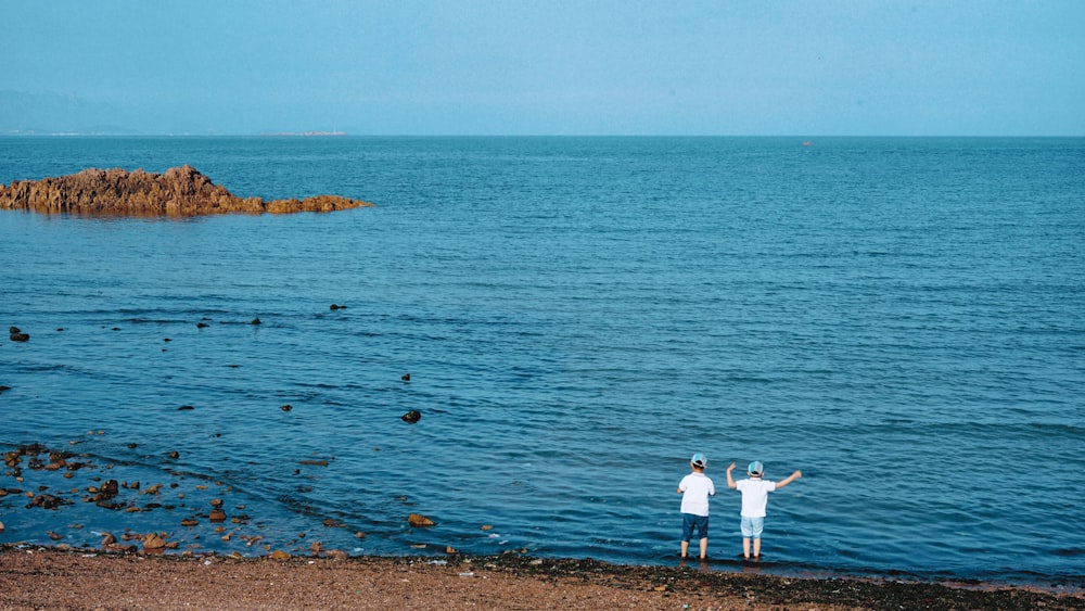 two children standing in front of body of water