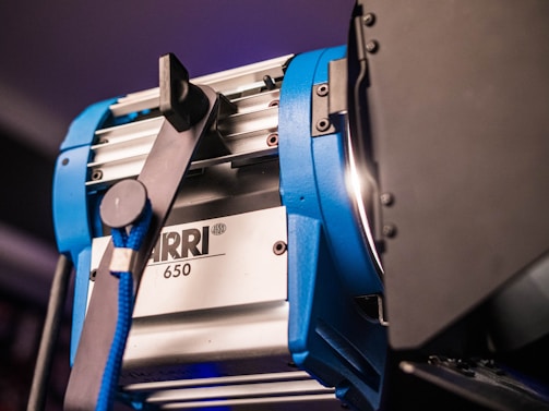 A professional studio light with a metallic finish and blue accents, featuring the brand ARRI and model number 650. The light is mounted on a stand with a black barn door attachment, likely used for controlling the direction of the light.
