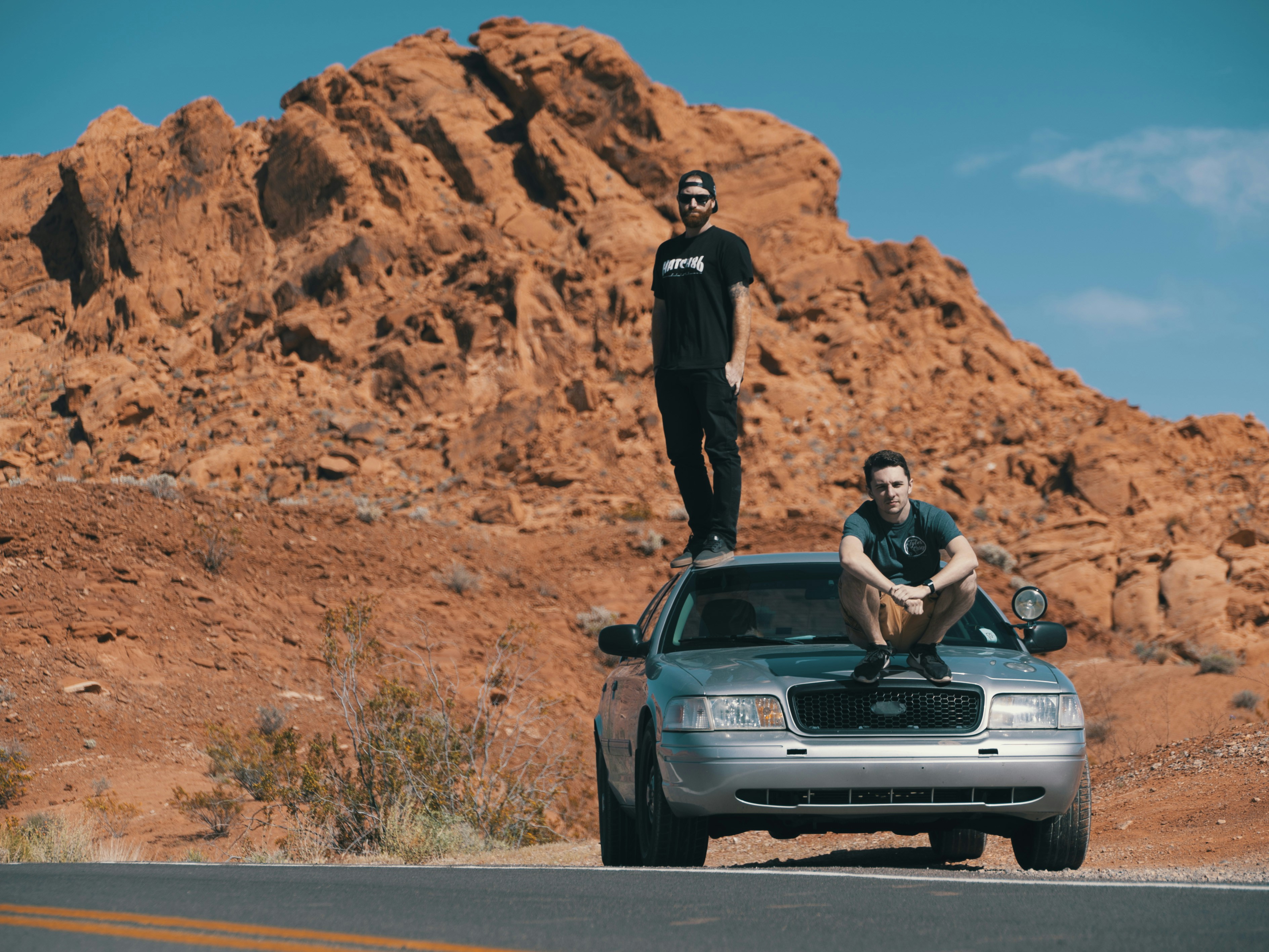 2 Filmmakers sitting and standing on a crown vic in the desert