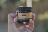 A hand holding a small glass jar of organic herbal oil.